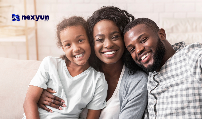 Família sorridente abraçada no sofá, ilustrando a escolha de um plano de saúde com bom preço em 2026